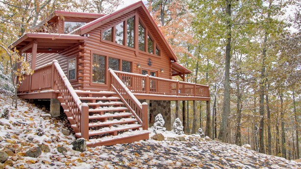Eine Blockhütte mit Balkon, Treppe und Blick auf den Wald.