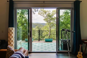 Quarto com uma grande porta de vidro deslizante que dá para uma varanda com vista para vegetação e colinas.