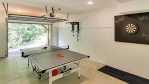 A ping pong table with a red paddle, a dartboard, and a ceiling-mounted projector. - Modern Fairview Retreat: Spacious Deck + Mtn View! (Fairview)