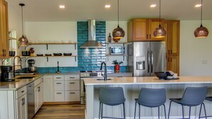 A modern kitchen with a central island, bar stools, wooden cabinets, and pendant lighting. - Modern Fairview Retreat: Spacious Deck + Mtn View! (Fairview)