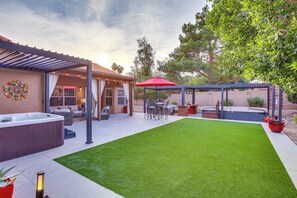A backyard with a hot tub, patio furniture, and a covered seating area.