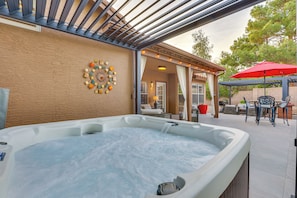 A hot tub with a pergola overhead, a patio area with outdoor furniture, and a decorative wall piece.