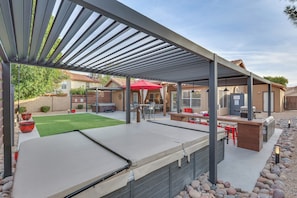 A covered outdoor patio with a pool table, seating area, and a barbecue setup.