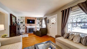 A living room with a fireplace, a sofa, a coffee table, and a television. - Historic Prescott Home w/ Yard & Fire Pit! (Prescott)