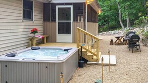 Een hottub buiten een huis met een houten terras, een barbecue en een houten omheining.