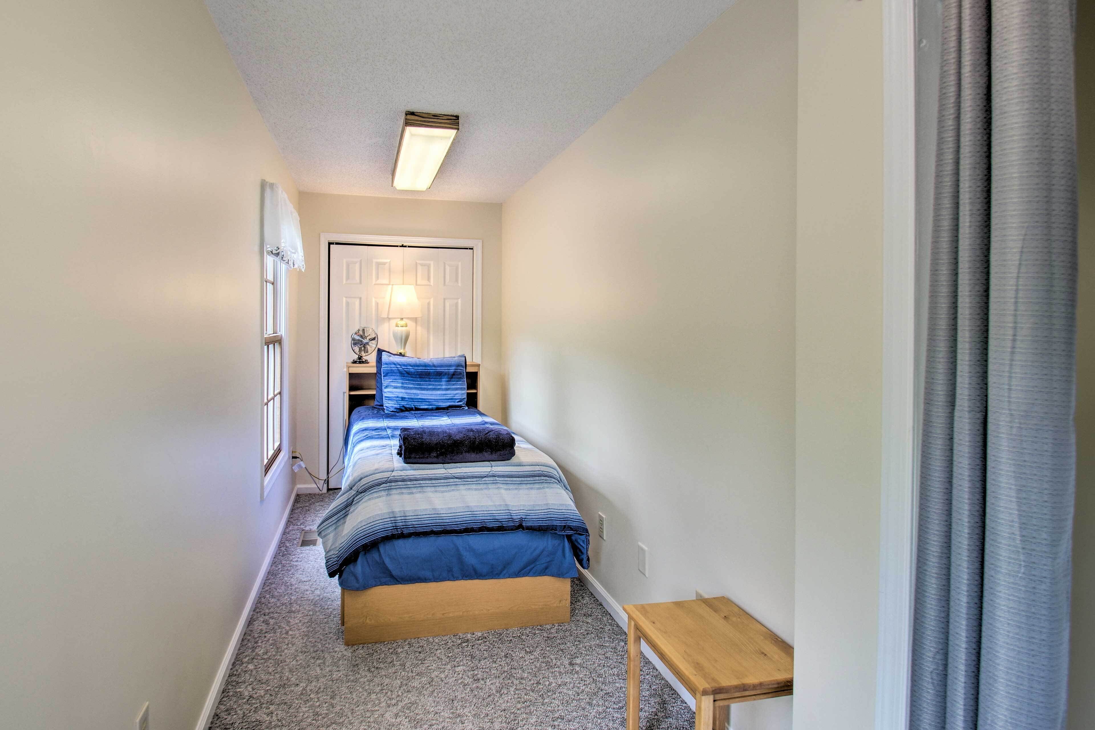 Un couloir étroit mène à une chambre à coucher qui contient un lit, une table de chevet et une lampe.