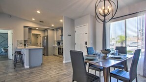 A modern kitchen with a central island, a dining area with a chandelier, and a large window with blinds.