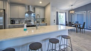A modern kitchen with a large island, bar stools, and a dining area with chairs and a table.