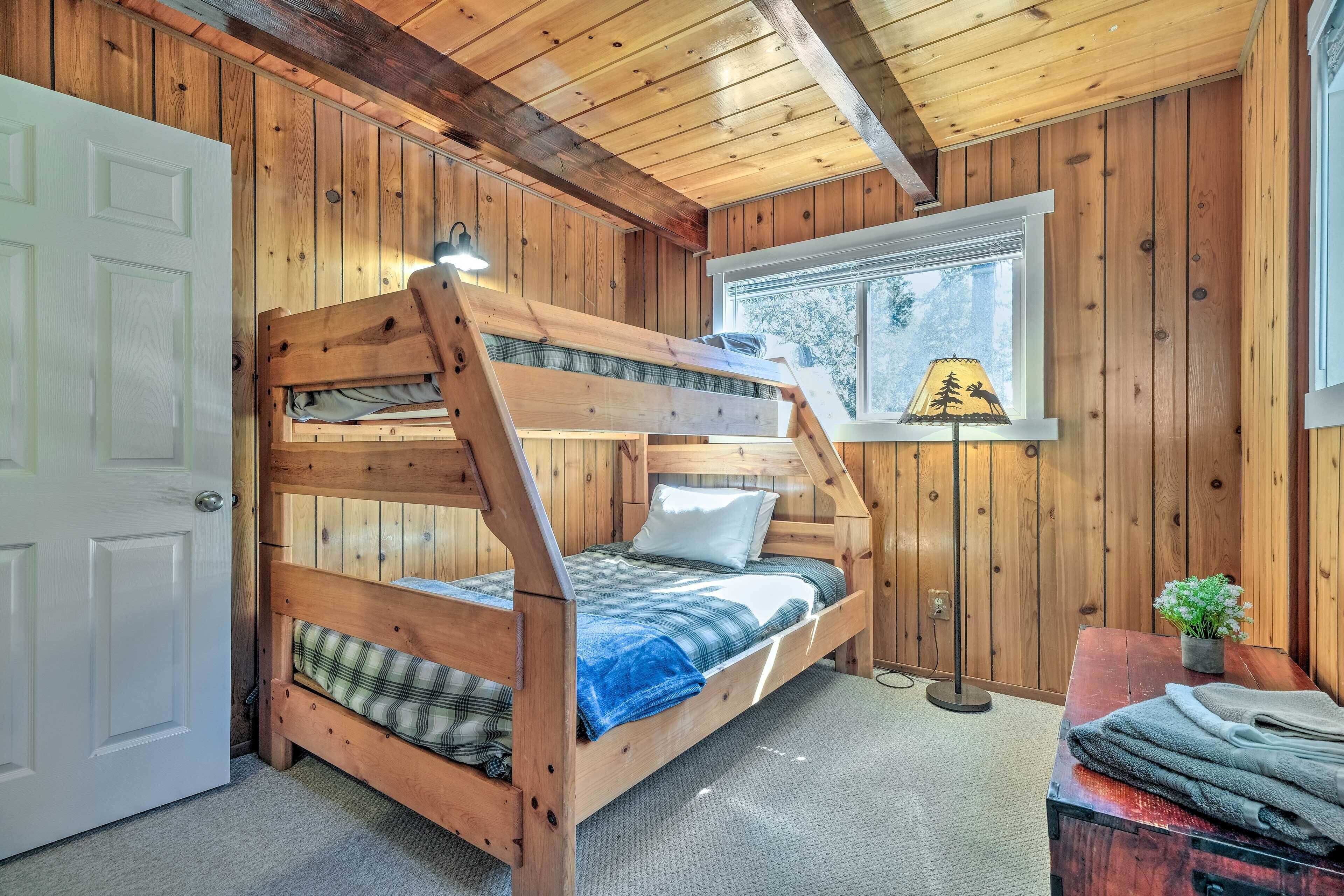 A bunk bed with a wooden frame, a window with a view of trees, and a lamp on a bedside table.