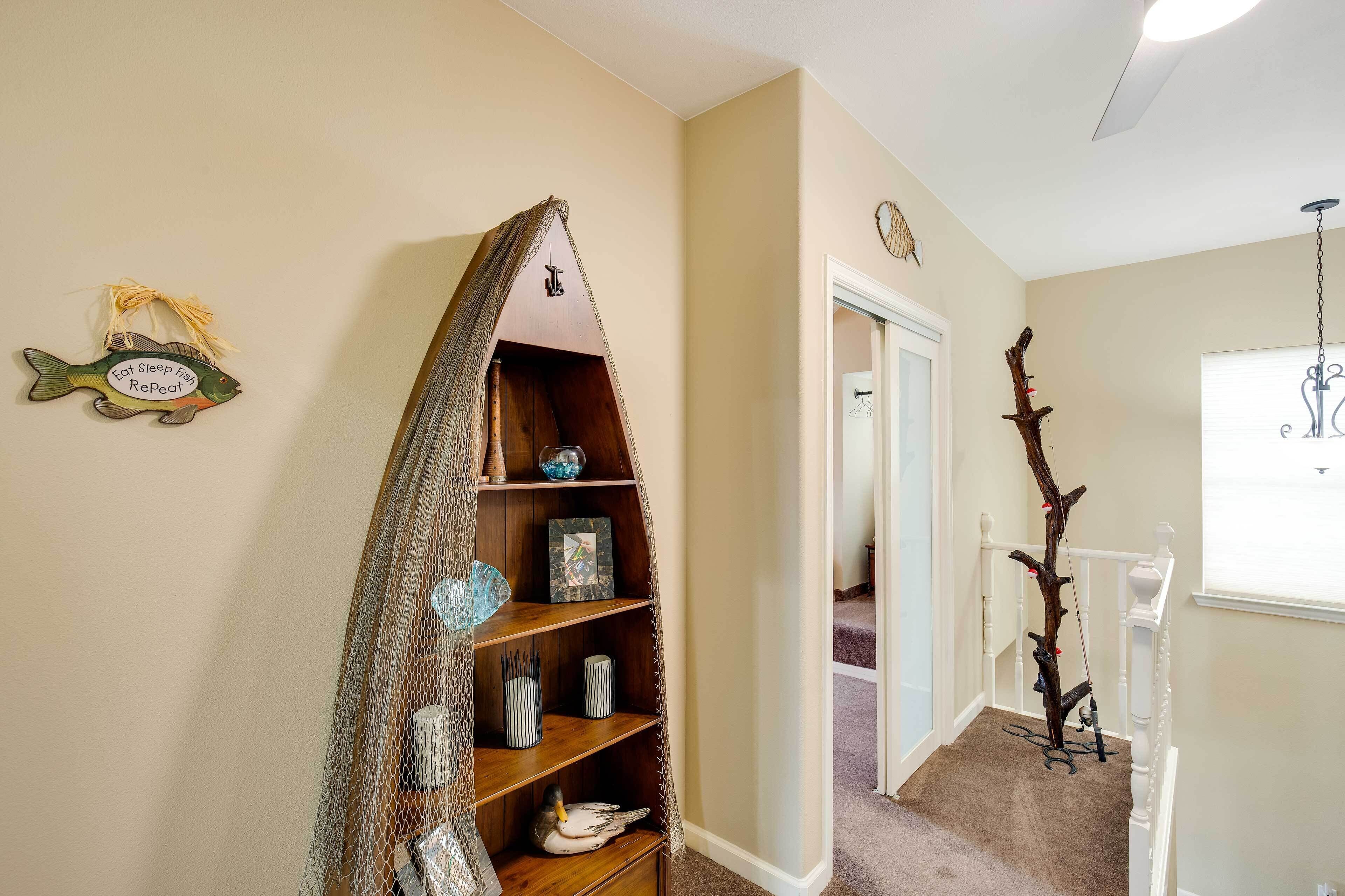 Un pasillo con un estante de madera con forma de pez que sostiene objetos decorativos, una silla de madera y un reloj de pared.