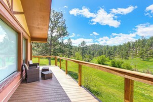 Una terraza de madera con mobiliario exterior, con vistas a un paisaje verde y árboles.