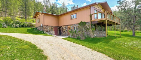 A two-story house with a stone foundation, a wooden deck, and a gravel driveway.