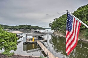 A dock with a small building, a flagpole with an American flag, and a river with greenery in the background. - Lakefront Haven: Family-friendly Sunrise Beach Gem (Sunrise Beach)