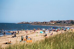 A beach with tents and umbrellas, a Ferris wheel, and buildings in the background.