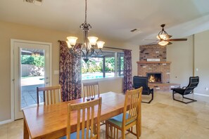 A dining area with a wooden table and chairs, a chandelier, a fireplace, and a ceiling fan. - Mesa Retreat: Pool, Hot Tub & Yard Near Downtown (Mesa)
