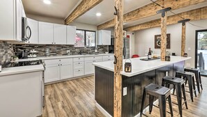 Een moderne keuken met witte kasten, een centraal eiland met krukken, en zichtbare houten balken.