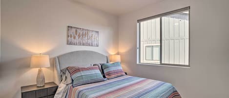 A bedroom with a bed, two bedside lamps, a ceiling fan, a window, and a wall-mounted artwork.