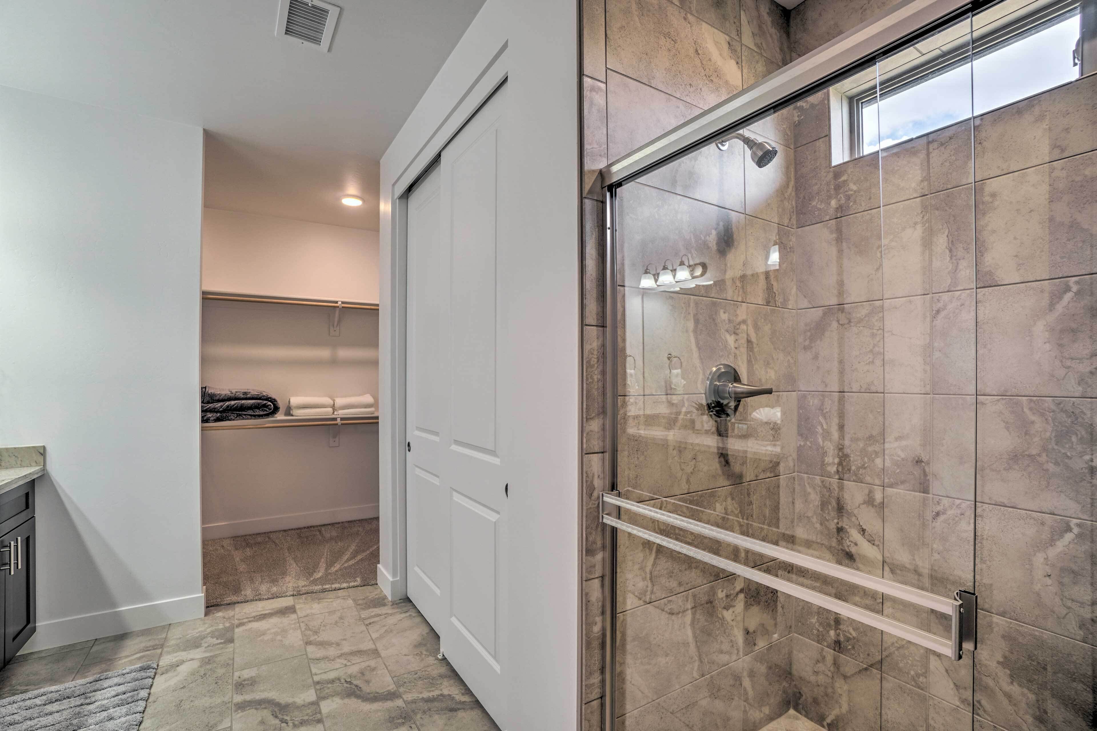 Un baño moderno con ducha de vidrio, azulejos de mármol, un perchero y un estante empotrado.