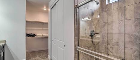 Un baño moderno con ducha de vidrio, azulejos de mármol, un perchero y un estante empotrado.