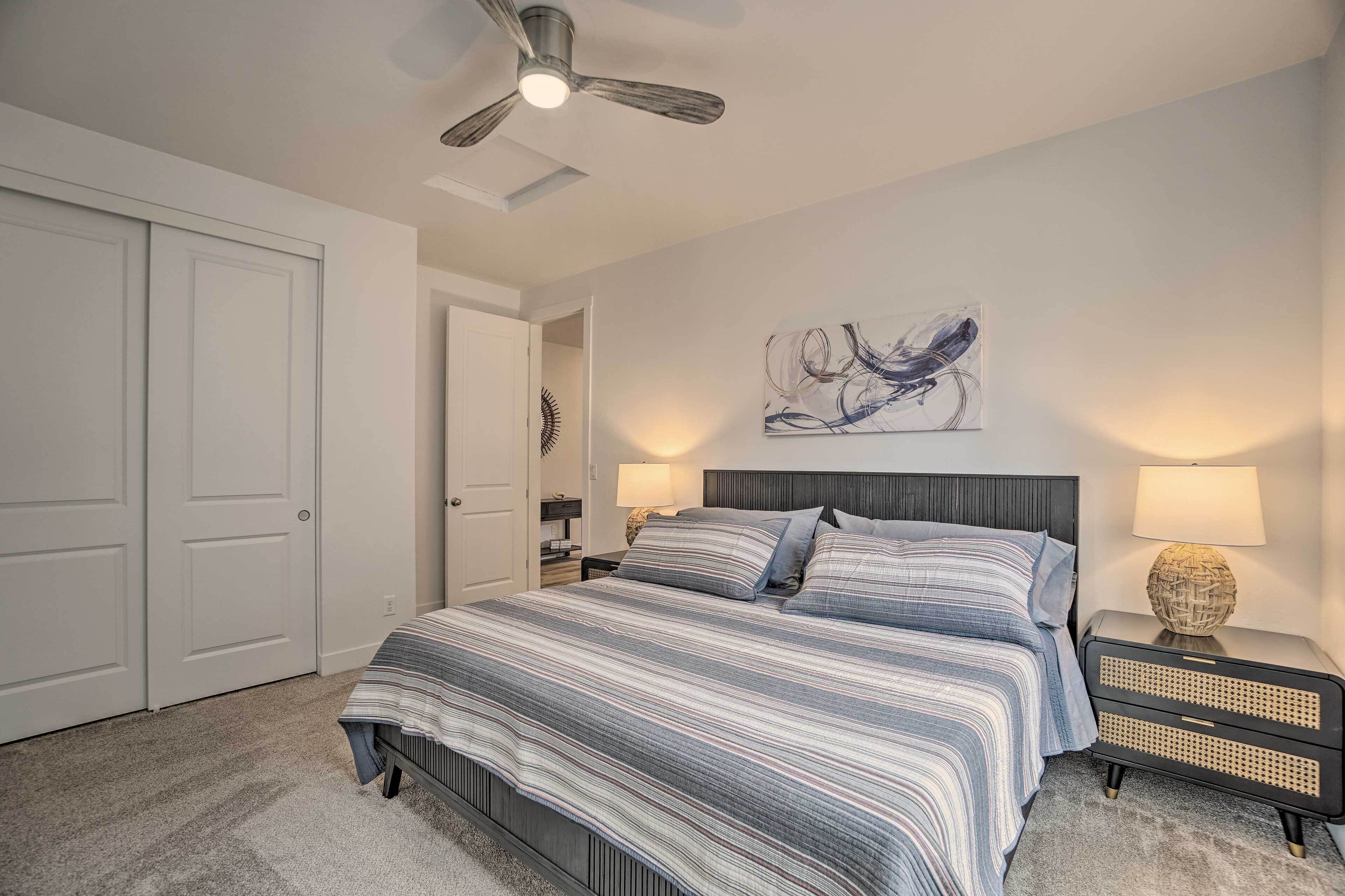 Une chambre à coucher comprenant un lit, un ventilateur de plafond, une œuvre d’art accrochée au mur et une table de chevet avec une lampe.