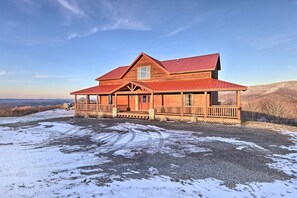 Situated on a gravel driveway, this cabin features a large front porch and a wooden deck.