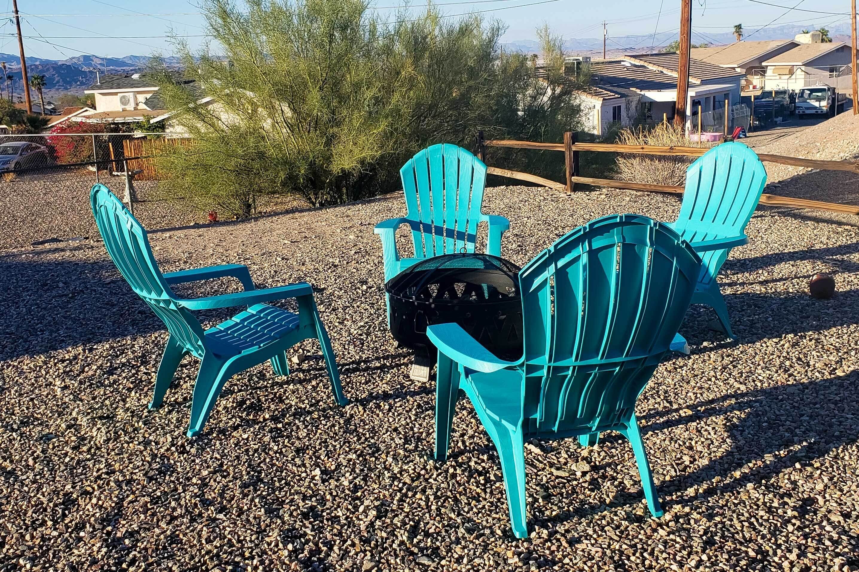 A set of turquoise Adirondack chairs on a gravel surface with a view of a residential area and mountains in the background.