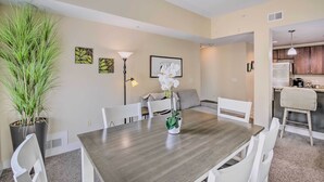 A dining area with a wooden table, white chairs, a potted plant, and artwork on the walls. - Grand Haven Condo w/ Patio < 1 Mi to Downtown (Grand Haven)