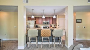 A modern kitchen with a central island, three bar stools, and pendant lighting. - Grand Haven Condo w/ Patio < 1 Mi to Downtown (Grand Haven)