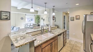 A kitchen with granite countertops, a stainless steel refrigerator, and pendant lighting. - Grand Haven Condo w/ Patio < 1 Mi to Downtown (Grand Haven)