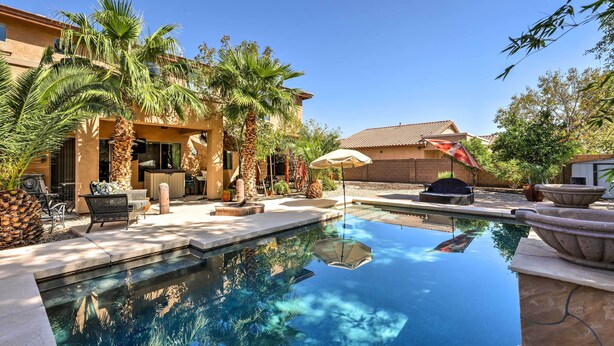 A swimming pool with a patio area, surrounded by palm trees and a building with a tiled roof.