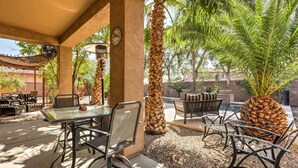 An outdoor patio with a glass table, metal chairs, a hammock, and a large potted plant.