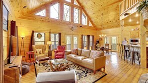 A spacious wooden cabin with a high ceiling, large windows, a cozy living area with a sofa and armchairs, a dining area, and a kitchen. - Spacious & Secluded Cabin: 25 Mi to Bentonville! (Sulphur Springs)