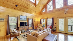 A spacious living room with wooden walls and floors, a large sofa, a television, and a deer mounted on the wall. - Spacious & Secluded Cabin: 25 Mi to Bentonville! (Sulphur Springs)