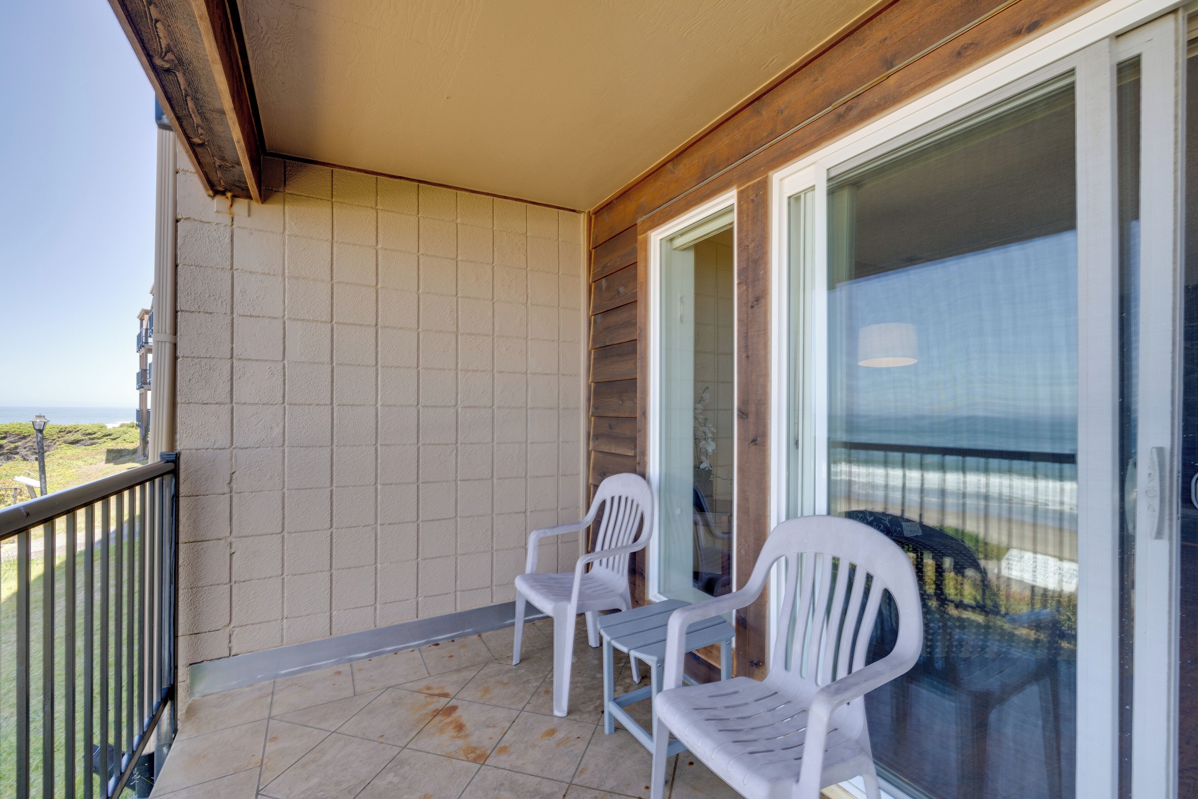 A balcony with two white plastic chairs, a glass door, and a view of the beach.