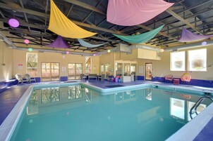 An indoor swimming pool with a clear view of the ceiling, windows, and poolside seating.