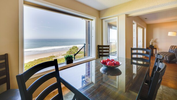 Un comedor con vistas a la playa, una mesa de vidrio y varias sillas.