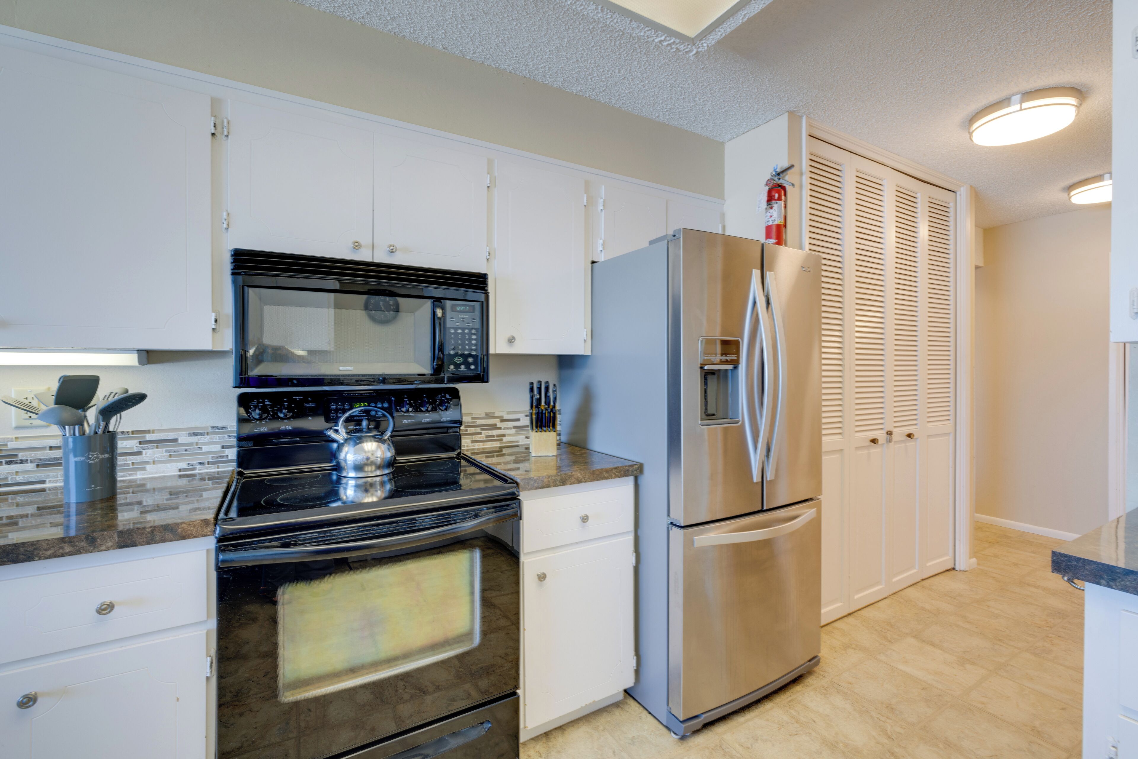 A modern kitchen with white cabinets, a stainless steel refrigerator, a microwave, and a stove.
