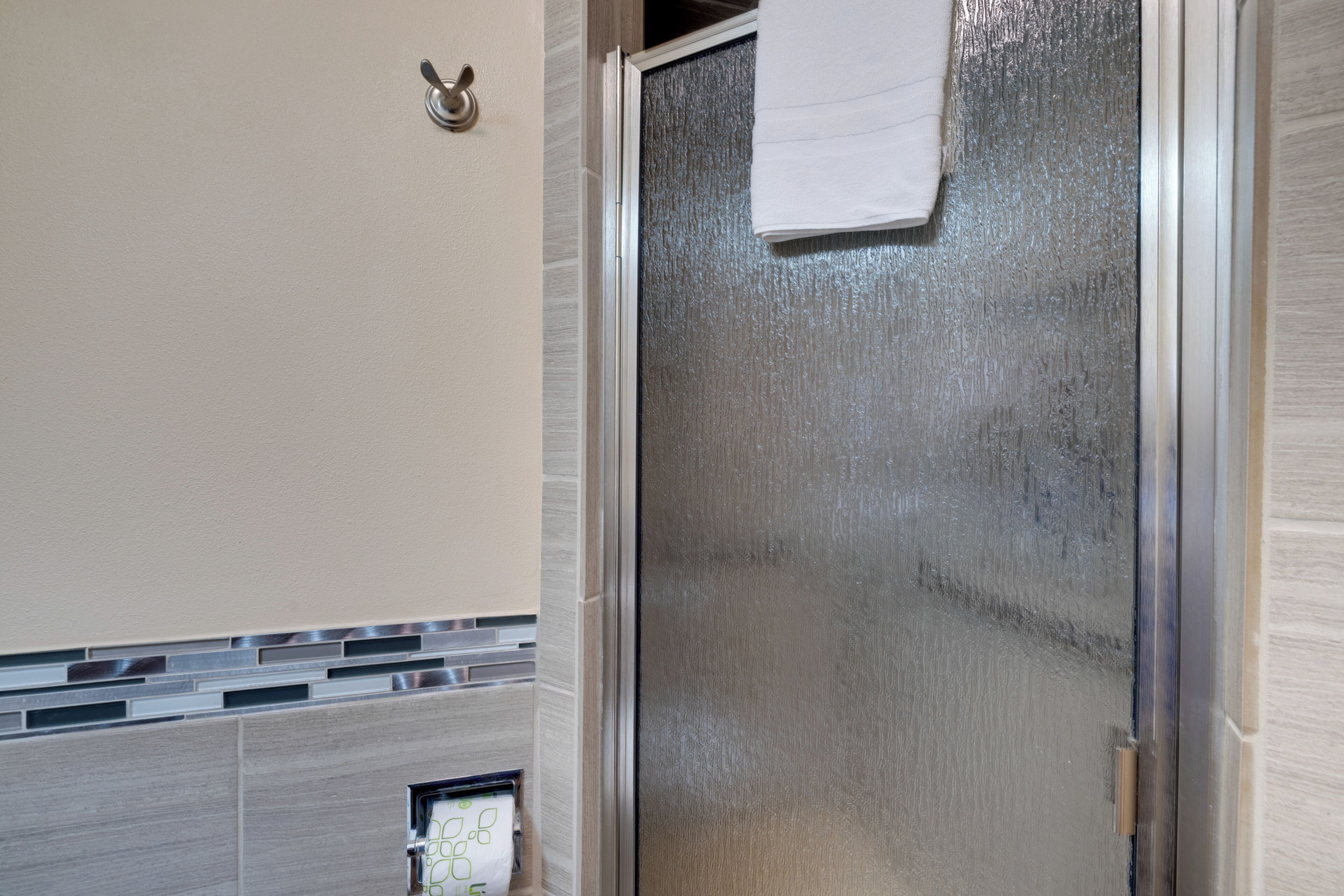 Een badkamer met een douchecabine van glas, een handdoek aan de deur en een handdoekhouder aan de muur.