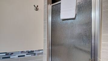 Een badkamer met een douchecabine van glas, een handdoek aan de deur en een handdoekhouder aan de muur.