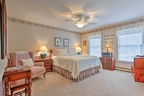 Ein Schlafzimmer mit einem Bett, einem Sessel, einem Nachttisch, einer Lampe und einem Deckenventilator.