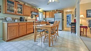 A kitchen with wooden cabinets, a dining table, chairs, a ceiling fan, and a refrigerator. - Charming Owls Head Retreat: 2 Mi to Rockland Coast (Owls Head)
