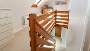 Quarto com escada de madeira, cômoda branca, radiador, janela e um quadro na parede.