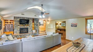 A cozy living room with a stone fireplace, a large flat-screen TV, and a comfortable gray sectional sofa. - Family-friendly House: Fish, Hike, Bike & More! (South Fork)