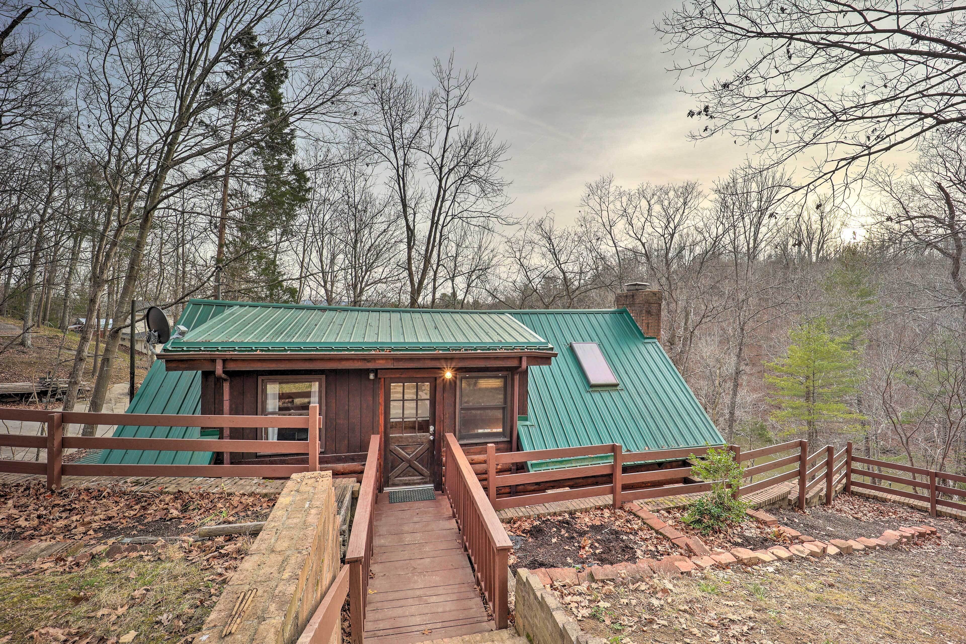 A cabin with a green roof, wooden deck, and a fenced entrance.
