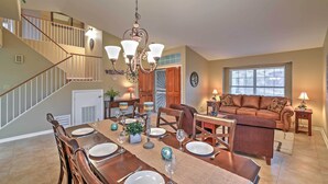 A spacious dining area with a wooden table set for four, a chandelier, and a staircase leading to an upper level. - Hot Tub & Pool: Stunning Goodyear Home Near Lakes (Goodyear)