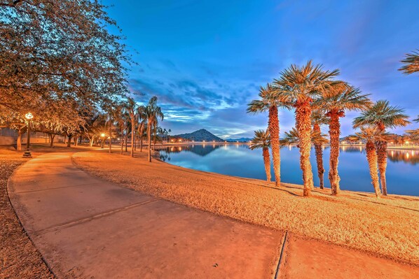 A waterfront promenade with palm trees, a calm lake, and a mountain in the background. - Hot Tub & Pool: Stunning Goodyear Home Near Lakes (Goodyear)