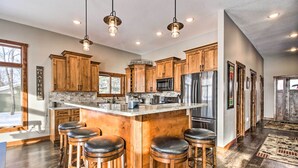 A modern kitchen with wooden cabinets, a central island with stools, stainless steel appliances, and pendant lighting. - Cabin w/ Gradual Slope to Sandy Bottom Swimming! (Siren)