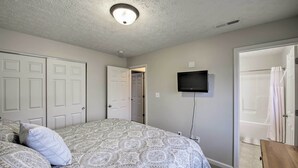 Quarto com colcha estampada, televisão fixada na parede e porta de acesso a um banheiro.
