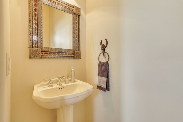 Ein Badezimmer mit weißem Waschbecken, einem Spiegel mit dekorativem Rahmen und einem Handtuch an einem Haken.