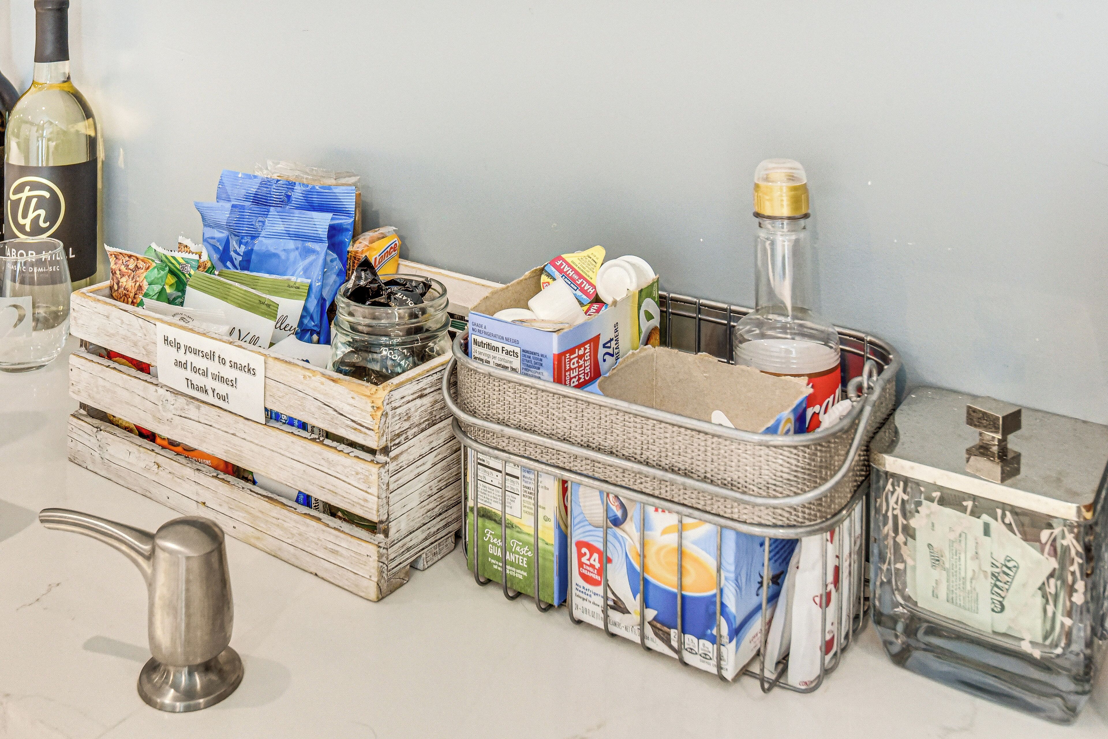 A kitchen counter with various food items, a bottle of wine, and a metal pitcher.
